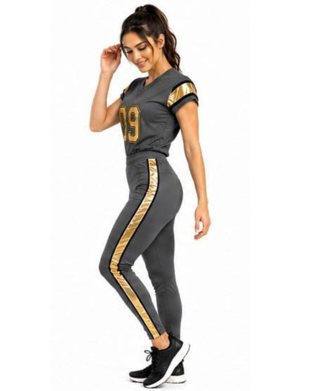 A woman modeling a dark gray athletic tracksuit with gold accents, featuring a short-sleeve top with gold lettering and matching high-waisted leggings with gold side stripes, set against a plain white background.