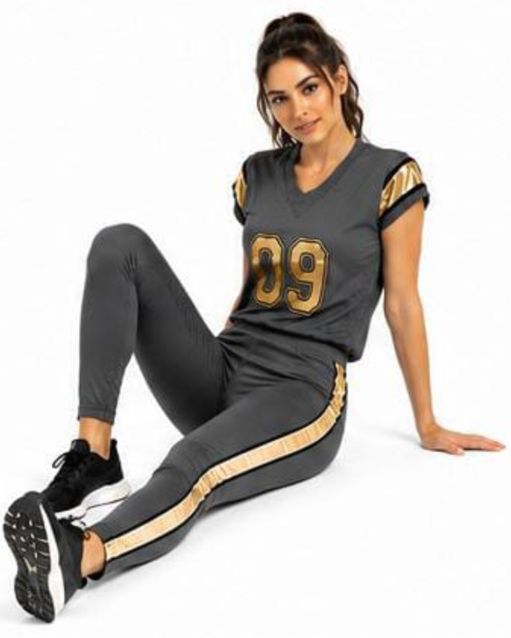 A woman wearing a dark gray athletic football-style jersey and matching leggings with gold number 99 and side stripes, posed against a plain white background.