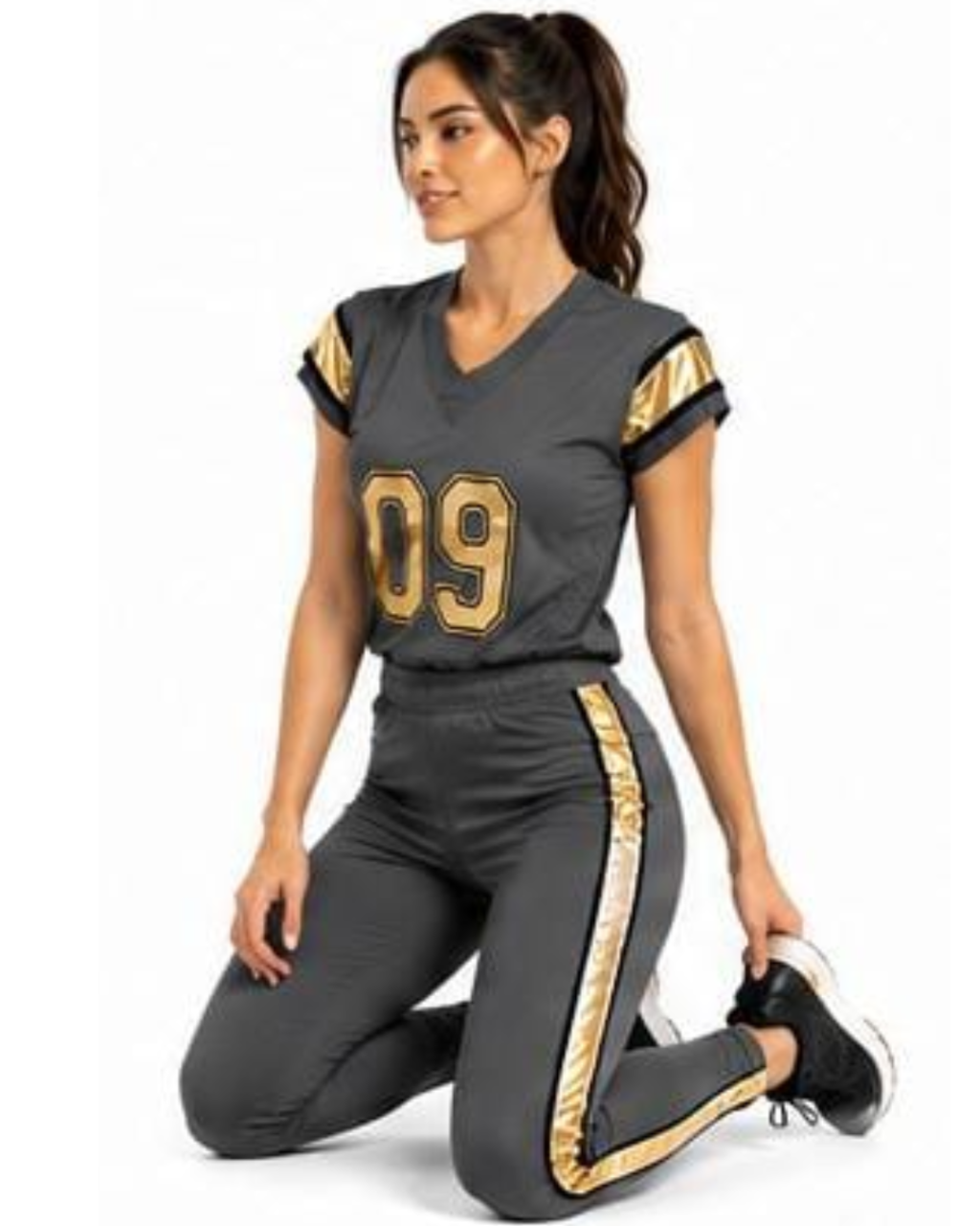 A woman kneeling on a white studio background wearing a dark gray football-style jersey with gold trim and the number 09, paired with matching dark gray pants with gold side stripes.
