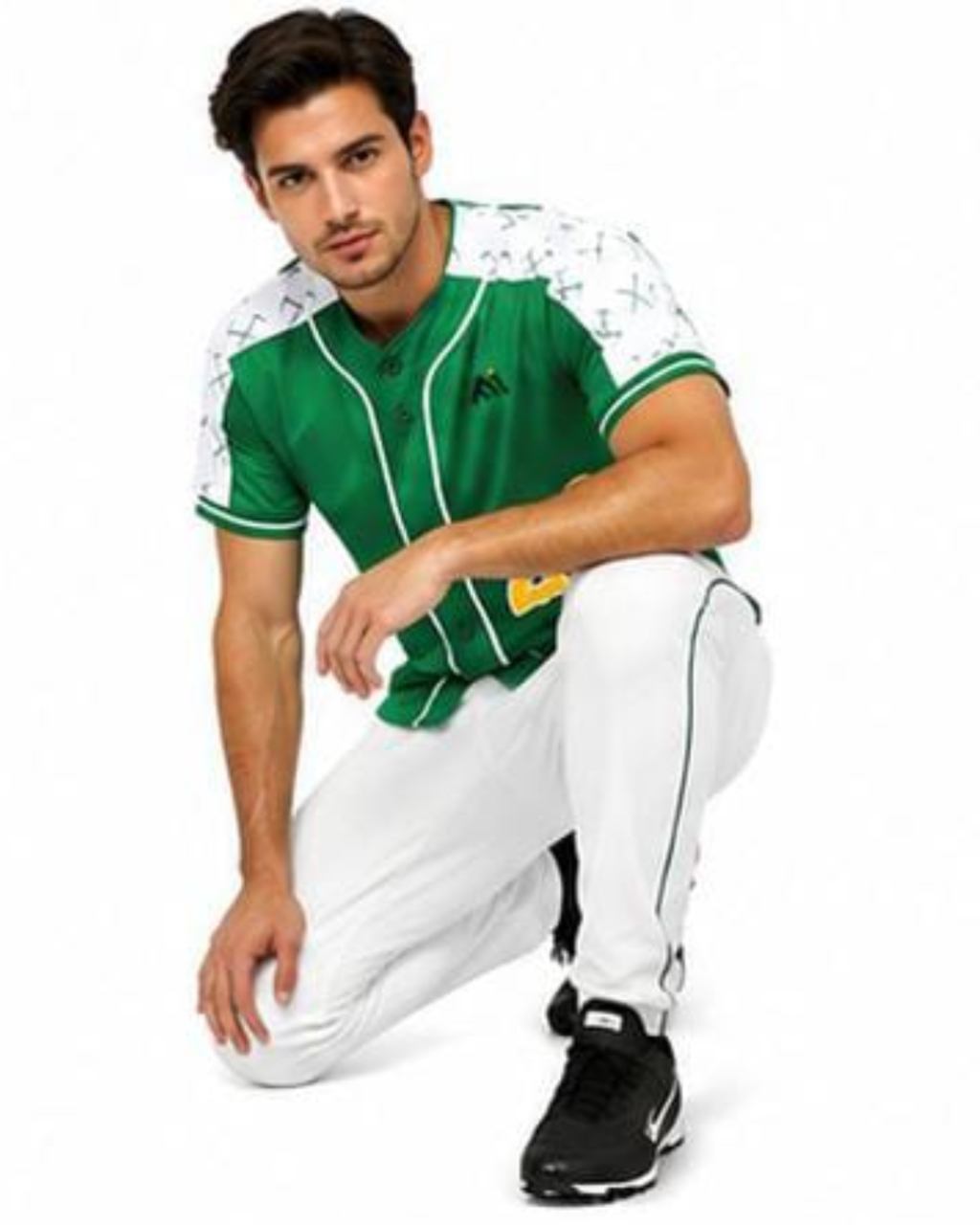 A man wearing a green and white baseball jersey with white pants and black sneakers, crouching in a studio setting against a white background.