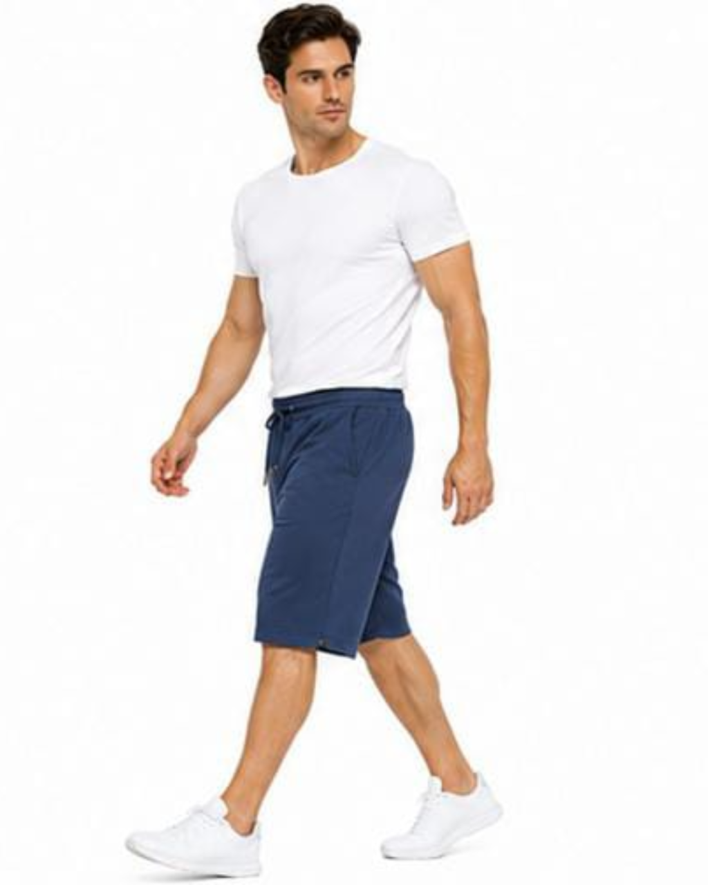 A man modeling a white crewneck t-shirt and navy blue knee-length athletic shorts with white sneakers, set against a plain white background.