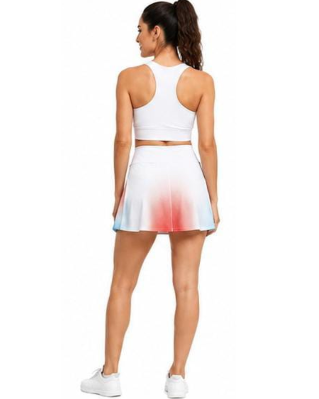 A woman shown from the back wearing a white athletic crop top and matching flared tennis skirt with a red and blue ombre gradient at the hem, paired with white sneakers, against a plain white background.