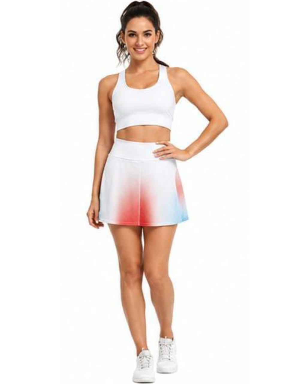A woman modeling a white athletic crop top and a matching high-waisted skater mini skirt with a red and blue ombre gradient at the hem, paired with white sneakers on a solid white background.
