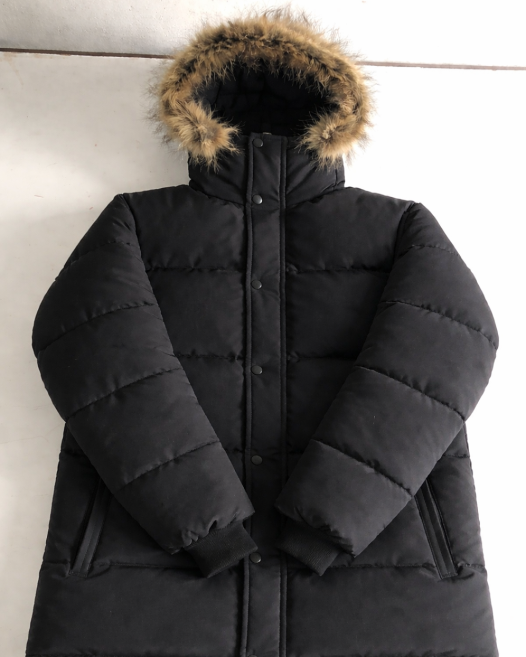 Black puffer coat with fur-lined hood on a light background
