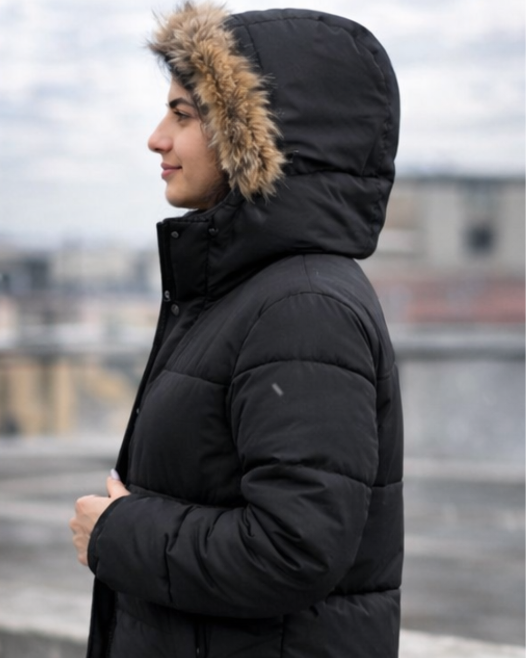 Person wearing a black puffer jacket with a fur-lined hood in an outdoor setting