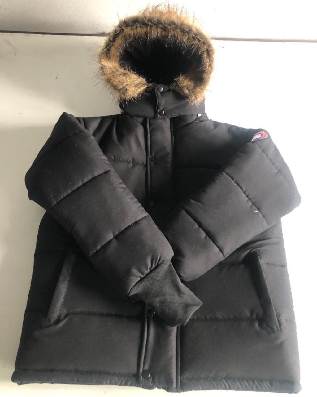 Black puffer coat with fur hood on a light wooden surface