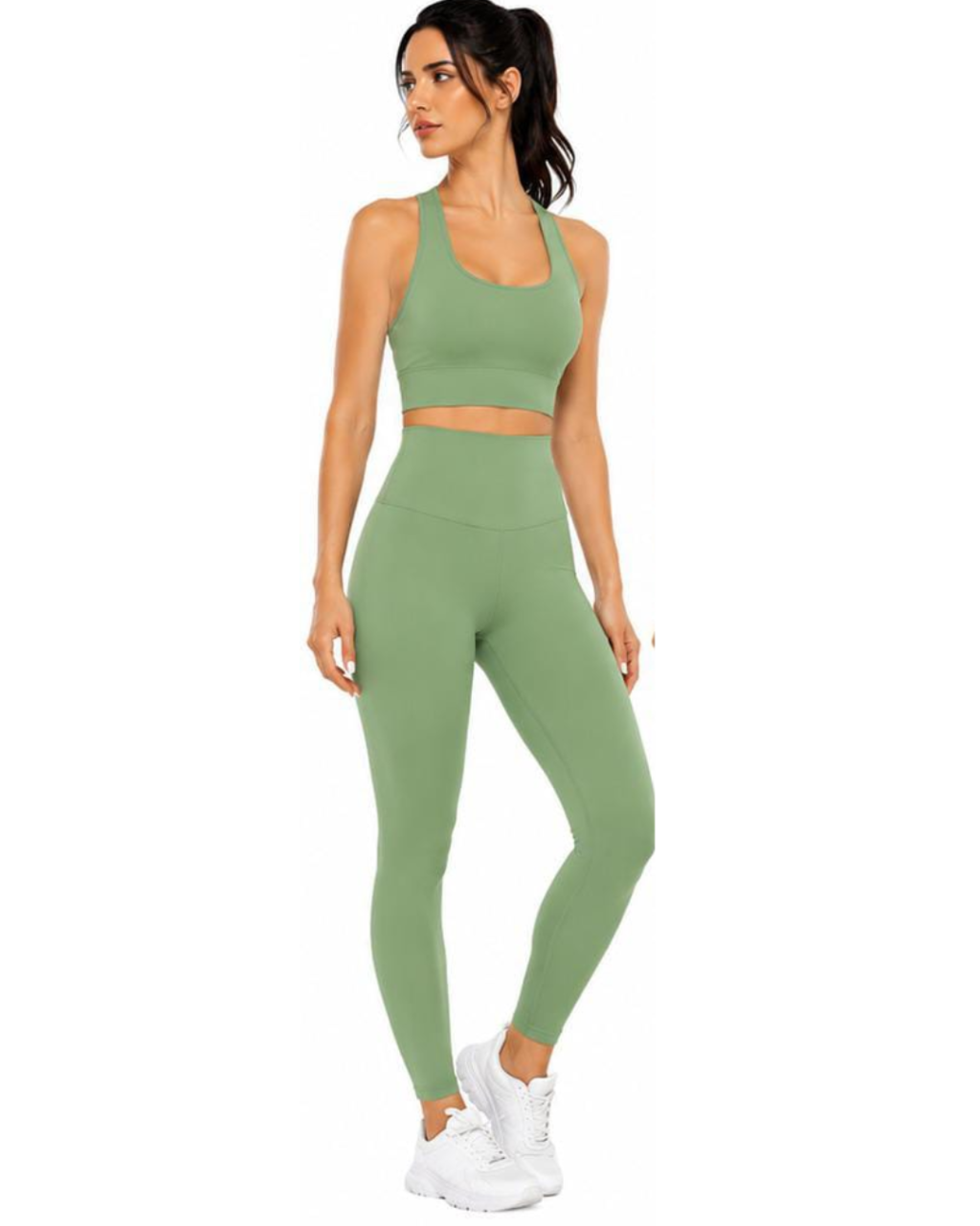 A woman modeling a matching sage green activewear set consisting of a sports bra and high-waisted leggings, paired with white sneakers, against a plain white background.