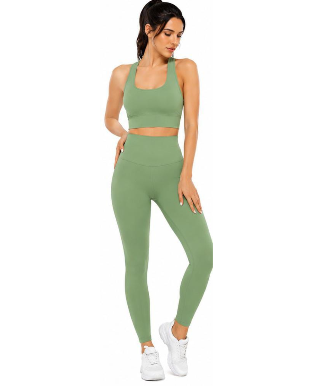 A woman modeling a matching sage green activewear set consisting of a sports bra and high-waisted leggings, paired with white sneakers, against a plain white background.