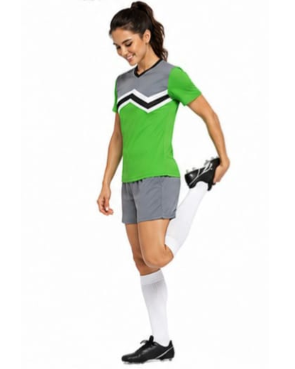 A woman modeling a green and gray athletic soccer uniform with a chevron pattern on the chest, gray shorts, white knee-high socks, and black cleats against a plain white background.