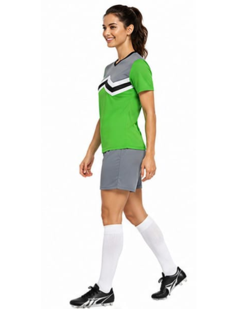 A woman modeling a green, gray, and white soccer jersey with matching gray shorts, white knee-high socks, and black soccer cleats against a plain white background.