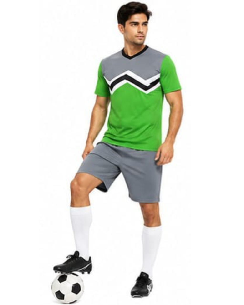 A man modeling a green and gray soccer jersey with a black and white chevron pattern, gray shorts, white socks, and black cleats, standing on a soccer ball against a white background.