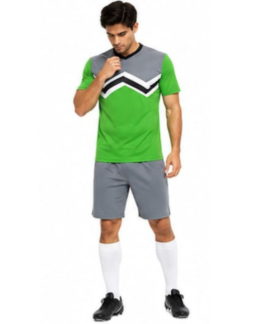 A man modeling a green and gray athletic soccer kit with a black and white chevron pattern on the chest, gray shorts, white socks, and black cleats, set against a plain white background.