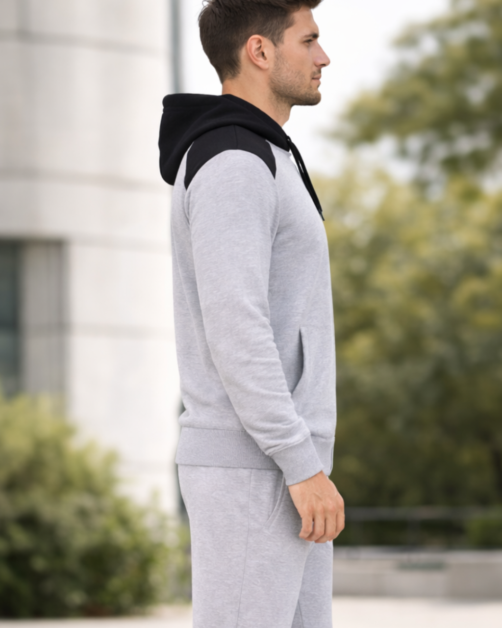 Man wearing a gray tracksuit with a black hood in an outdoor setting