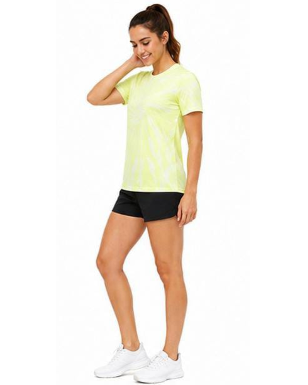 A woman modeling a short-sleeve athletic t-shirt in neon yellow-green with a white tie-dye pattern, paired with black athletic shorts and white sneakers, against a plain white background.