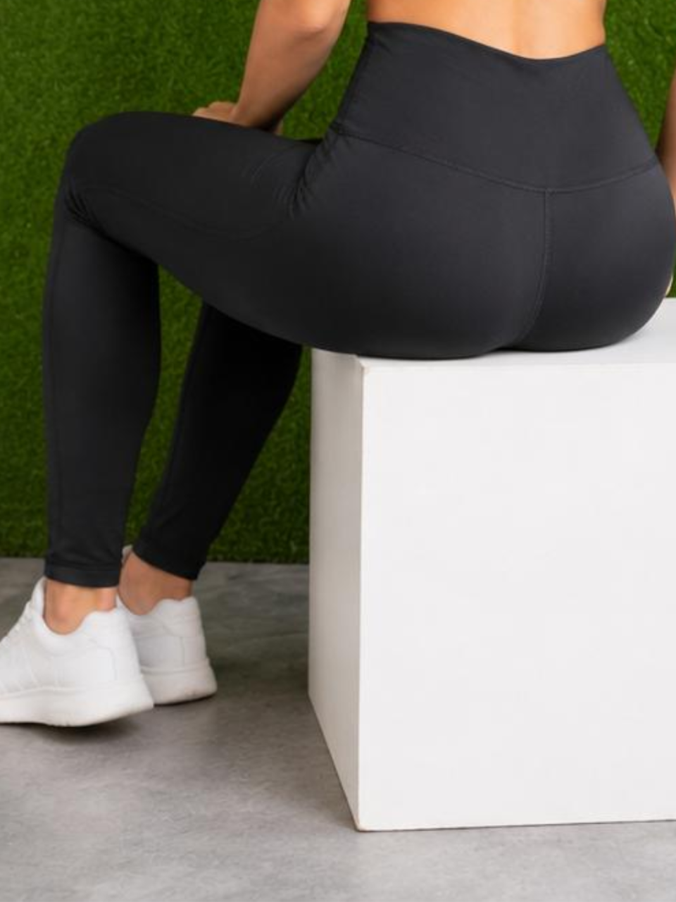Person wearing black leggings sitting on a white box with a green grass background