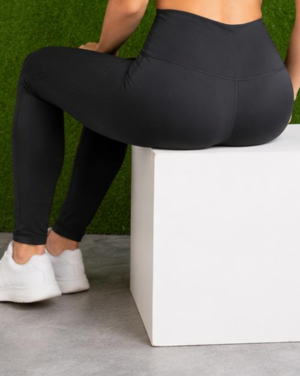Person wearing black leggings sitting on a white box with a green grass background