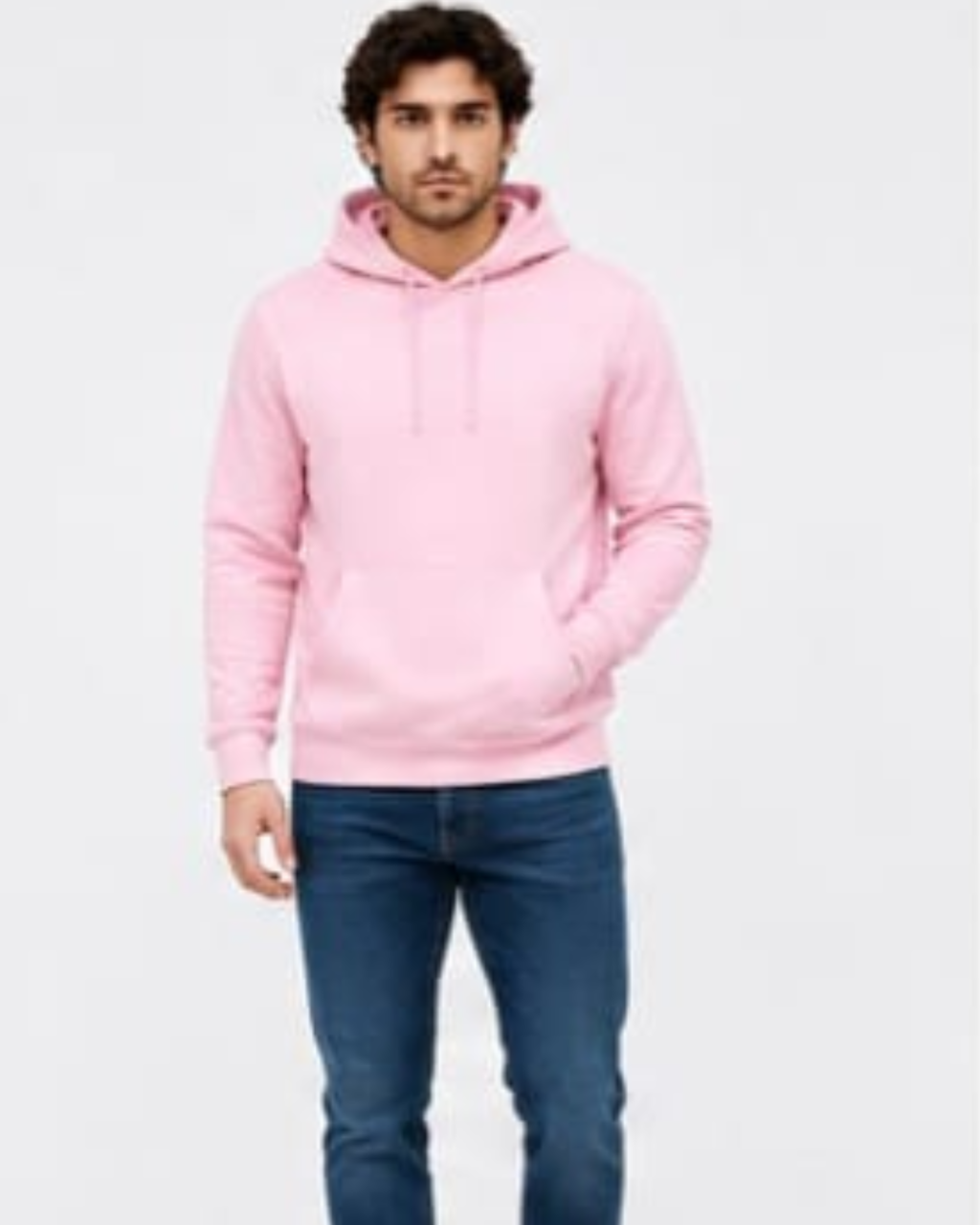A man wearing a light pink pullover hoodie with drawstrings and a front kangaroo pocket, paired with dark blue jeans, standing against a plain light gray background.