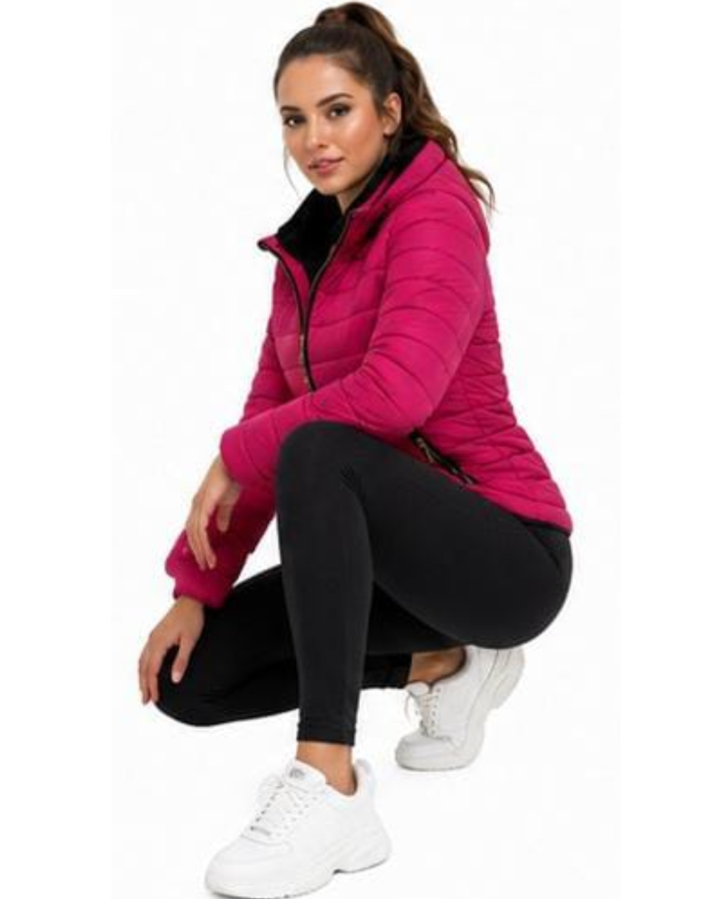 A woman crouching in a bright pink puffer jacket, black leggings, and white sneakers against a plain white background.