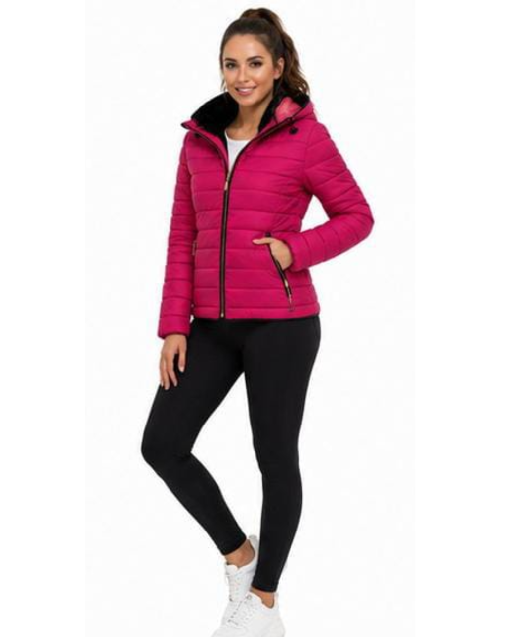 A woman modeling a bright pink puffer jacket with a black zipper and black lining, paired with black leggings and white sneakers, against a plain white background.