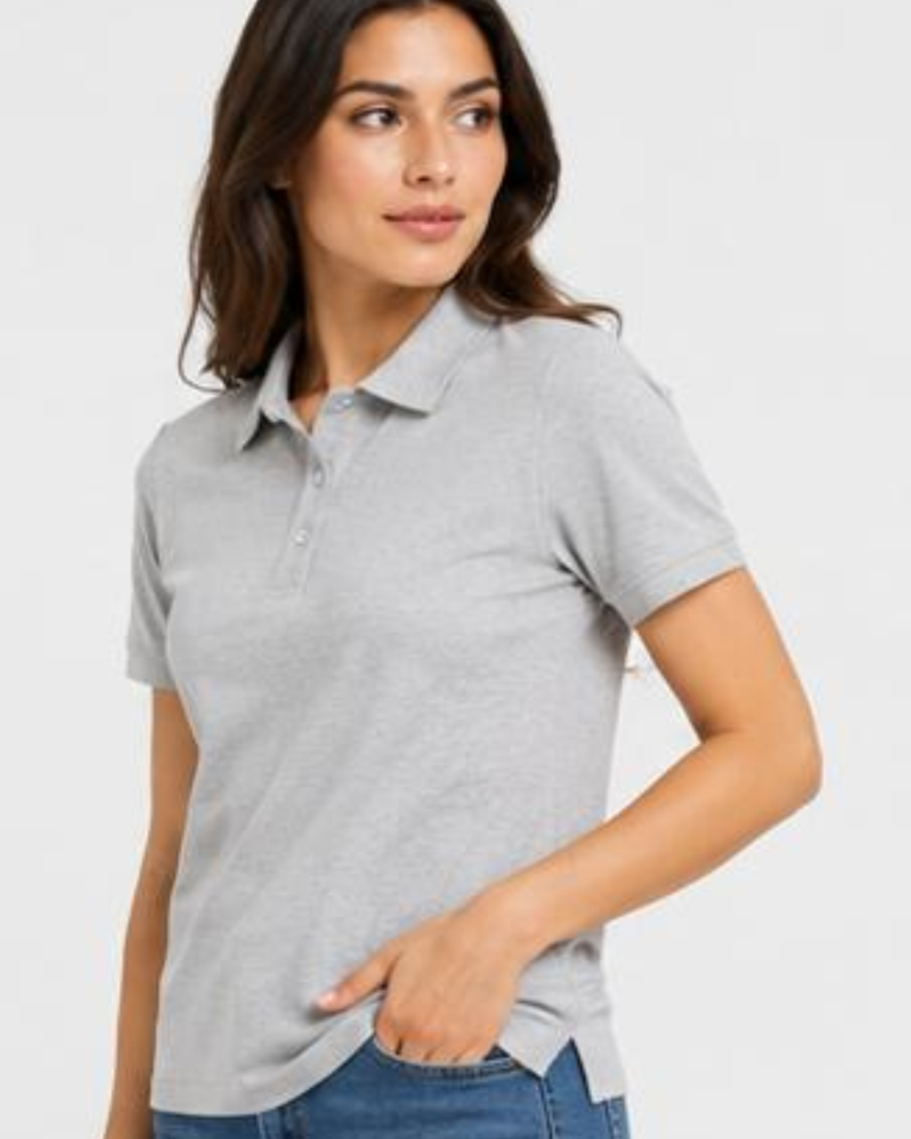 A woman wearing a light gray short-sleeve polo shirt with blue jeans, photographed against a plain light gray studio background.