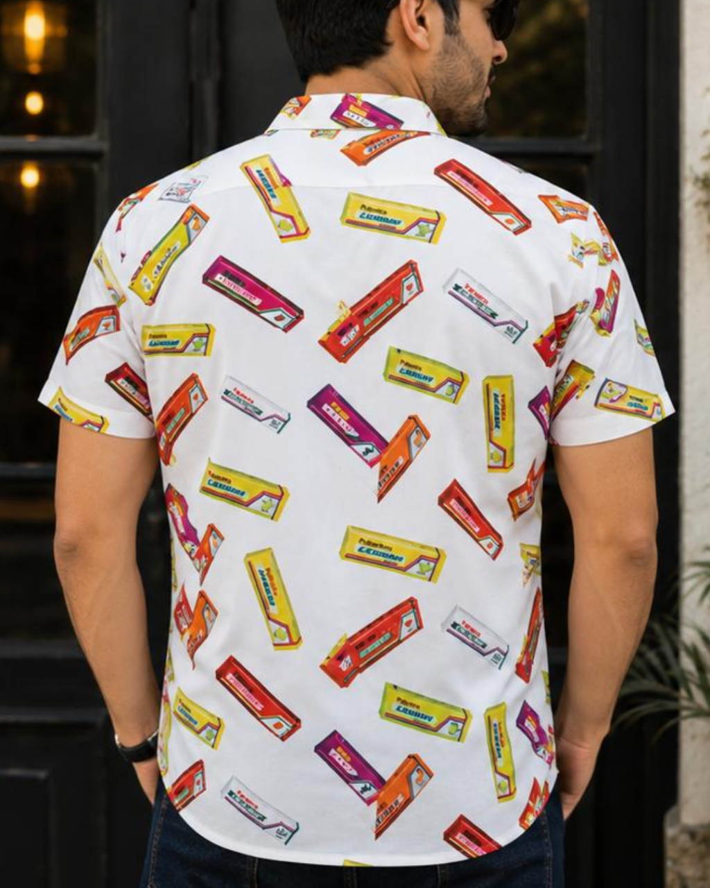 Man wearing a white shirt with colorful candy bar pattern outdoors.