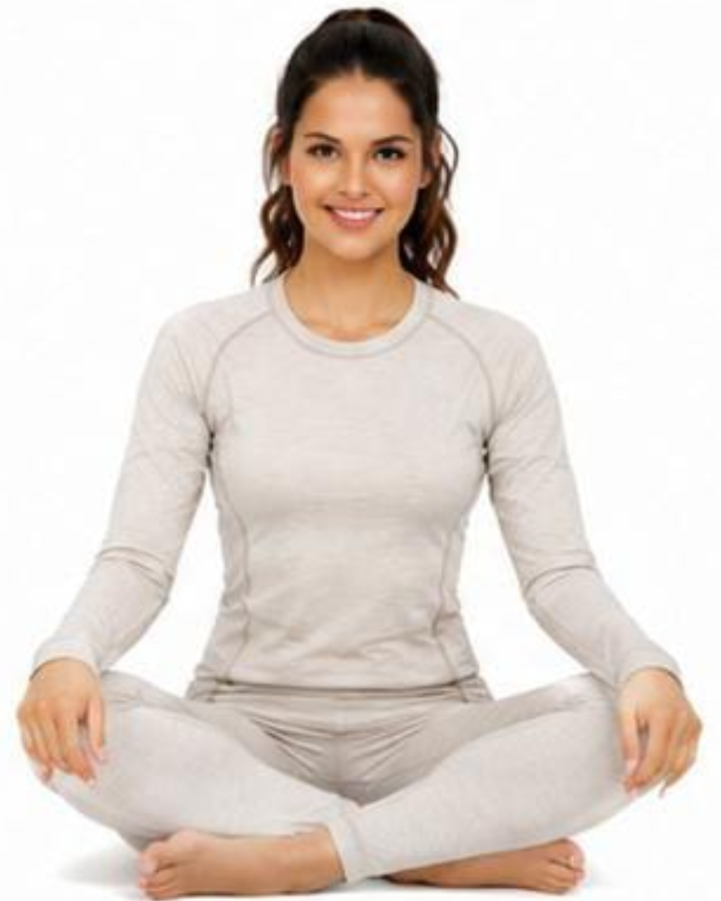 A woman sitting cross-legged in a light beige long-sleeve crewneck athletic top and matching leggings against a plain white background.