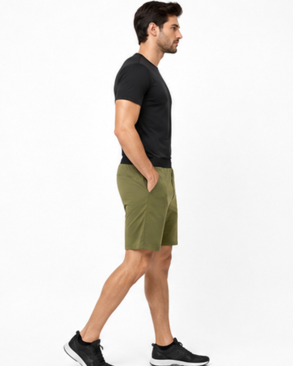 A man in side profile wearing a black short-sleeve t-shirt, olive green athletic shorts, and black sneakers, standing against a plain white studio background.