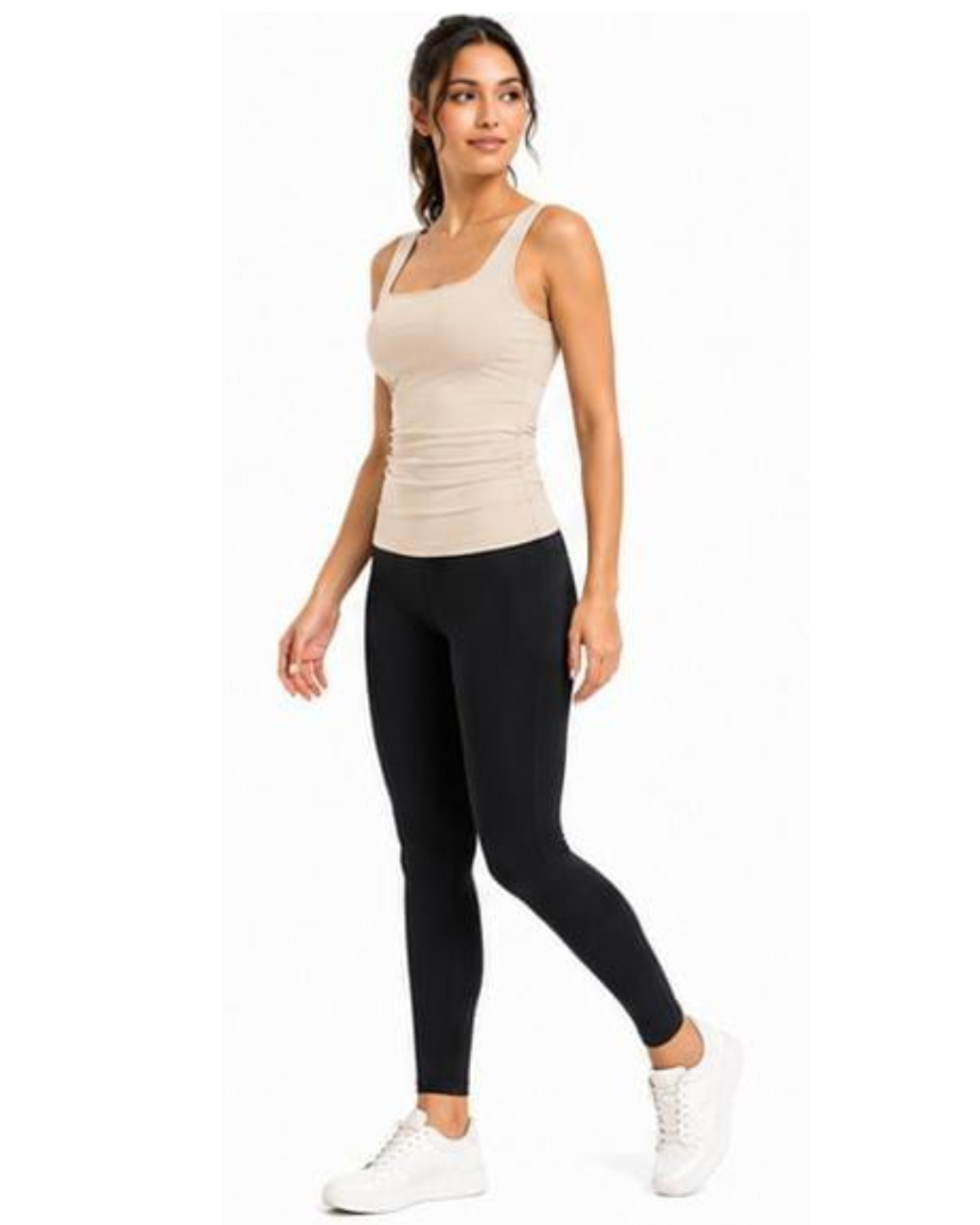 A woman modeling a beige ribbed tank top and black leggings with white sneakers, standing against a plain white background.