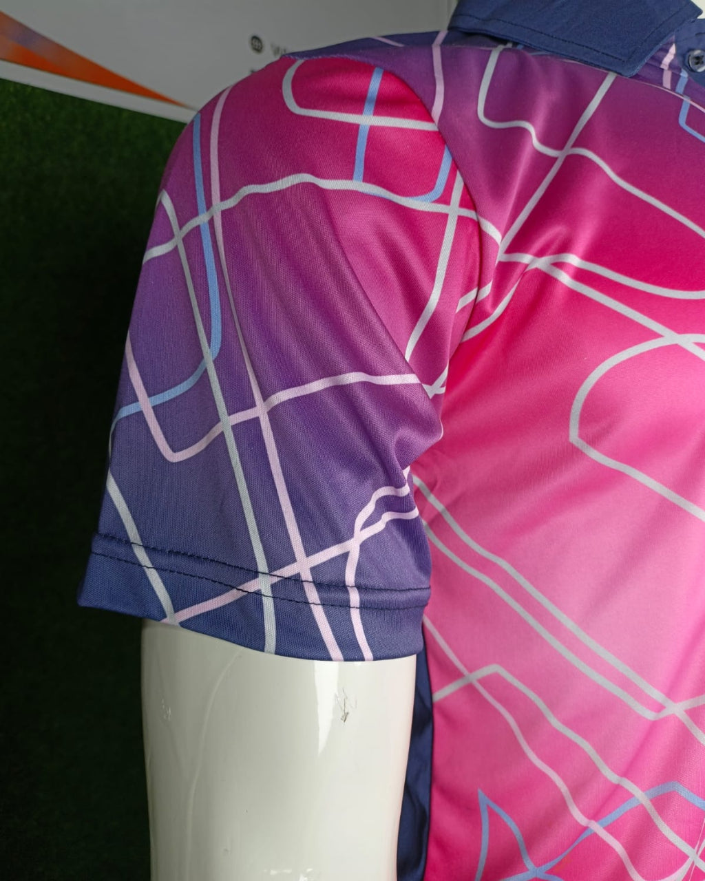 Close-up of a short-sleeve athletic polo shirt on a white mannequin torso, showing a pink-to-purple gradient with white and light blue geometric line patterns.