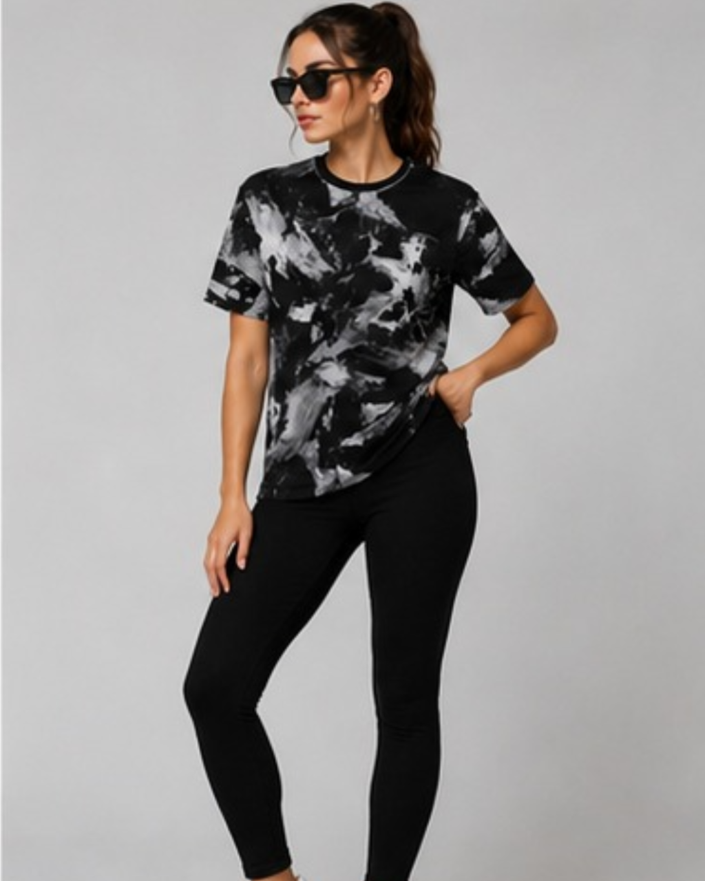 A woman modeling a black and white abstract patterned short-sleeve t-shirt paired with black leggings, standing against a solid gray studio background.