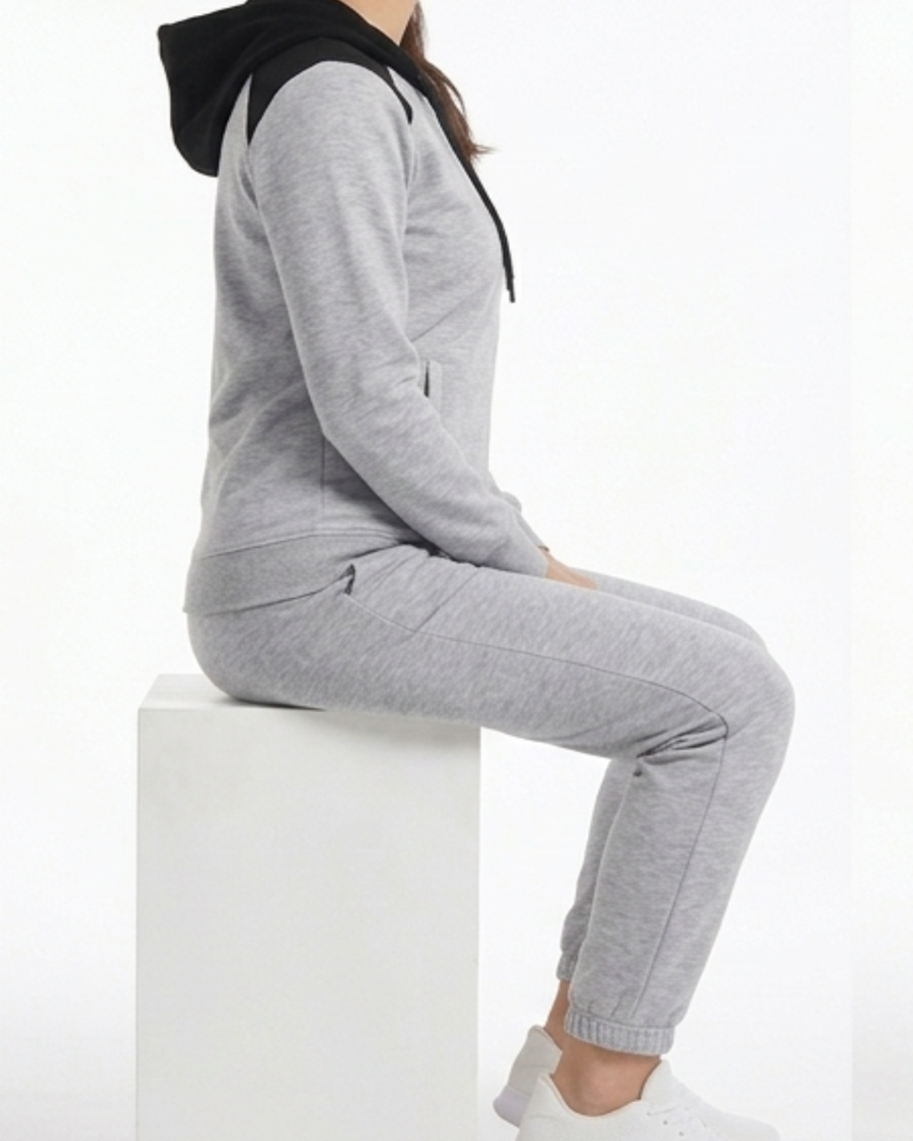 Person wearing a gray tracksuit sitting on a white block against a white background
