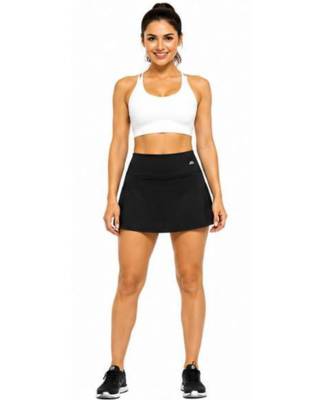 A woman modeling a white sports bra and a black athletic skort with white side stripes, standing against a plain white background.