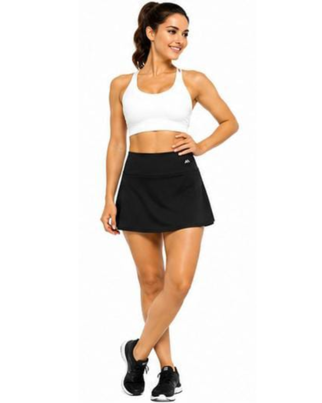 A woman modeling a white sports bra and a black athletic skort against a plain white background.