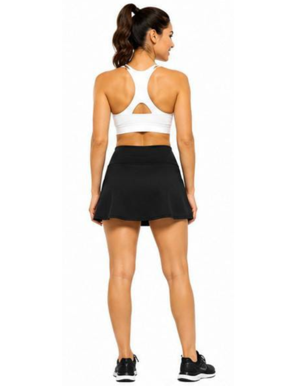 A woman shown from the back wearing a white sports bra with a cutout and a black athletic skirt, standing against a plain white background.