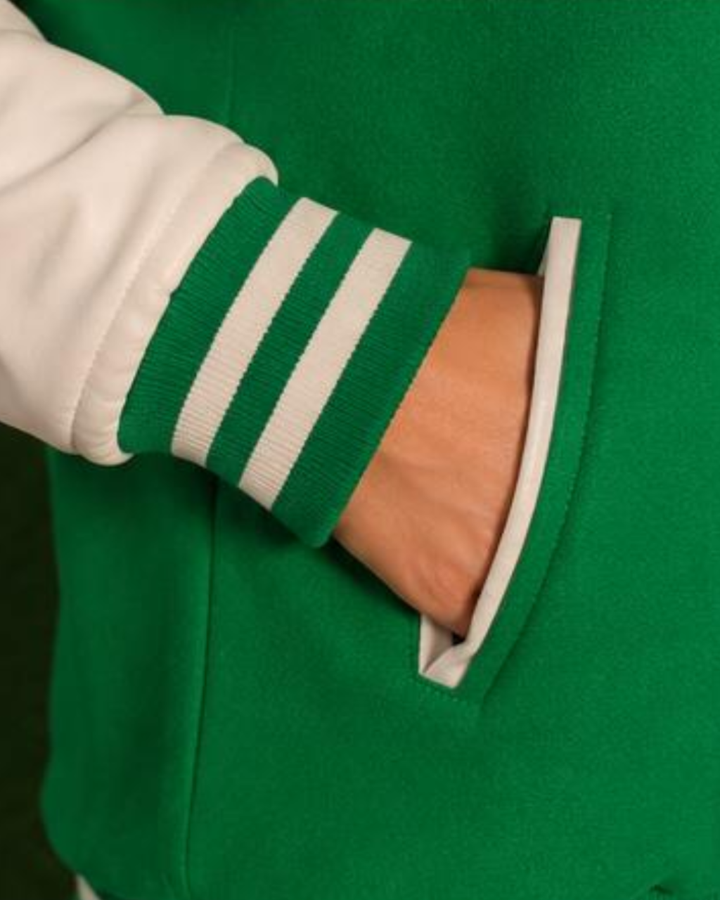 Green varsity jacket with white sleeves and collar, close-up of arm in pocket.