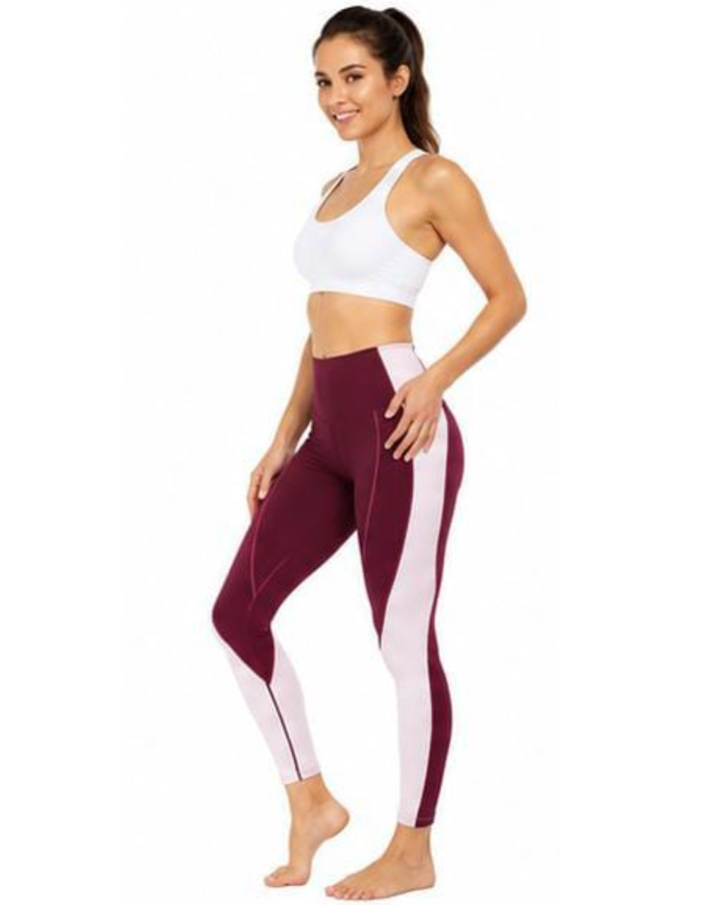 A woman modeling high-waisted colorblock leggings in burgundy and white, paired with a white sports bra, against a plain white background.