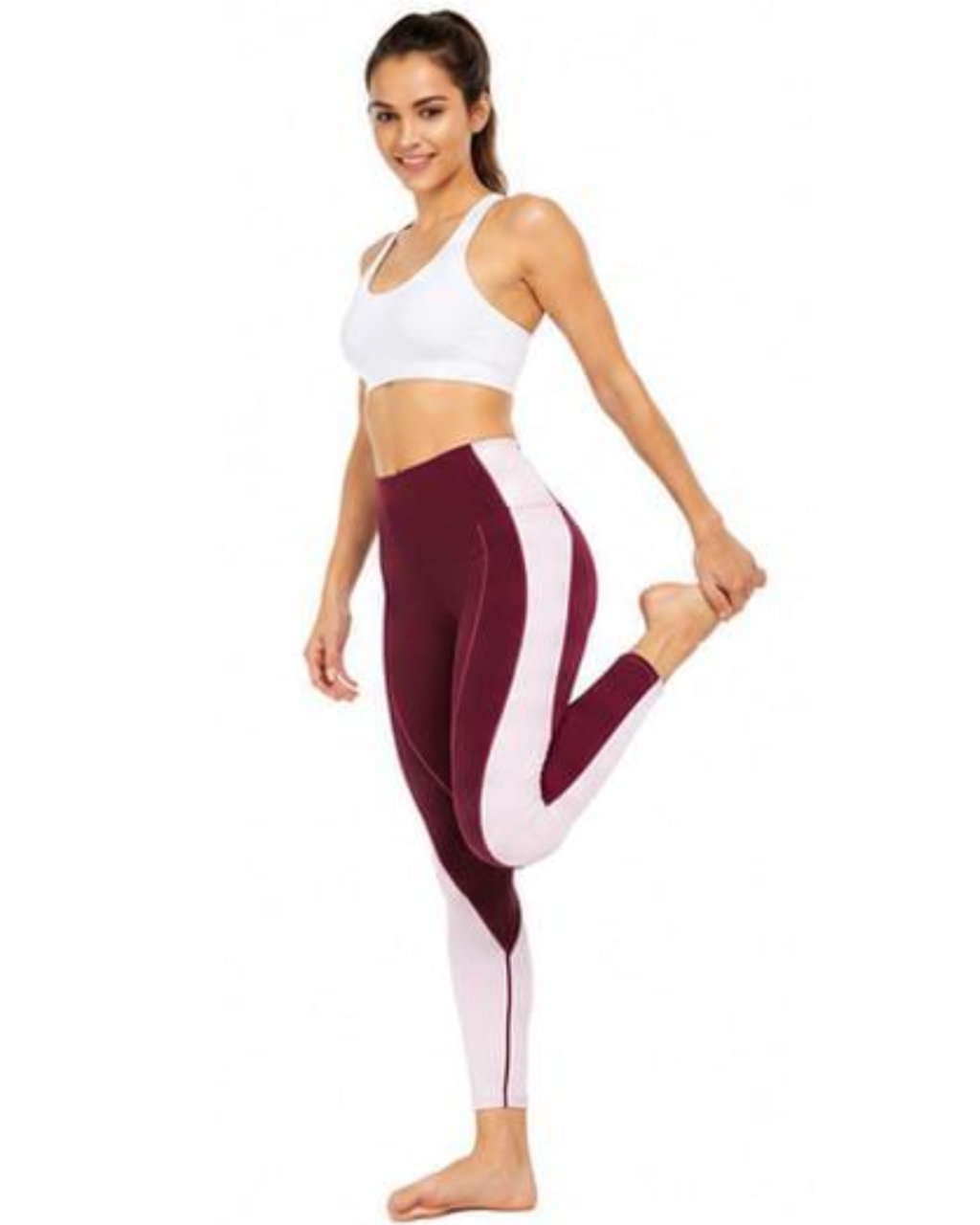 A woman modeling high-waisted colorblock leggings in burgundy and white, paired with a white sports bra, against a plain white background.