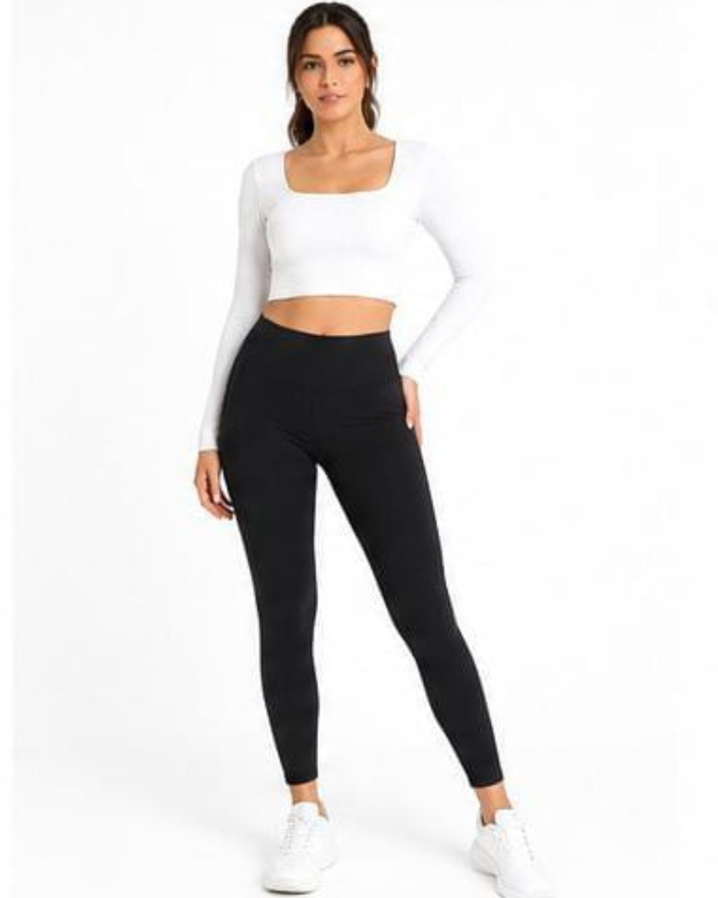 A woman modeling a white long-sleeve crop top and black high-waisted leggings against a plain white studio background.