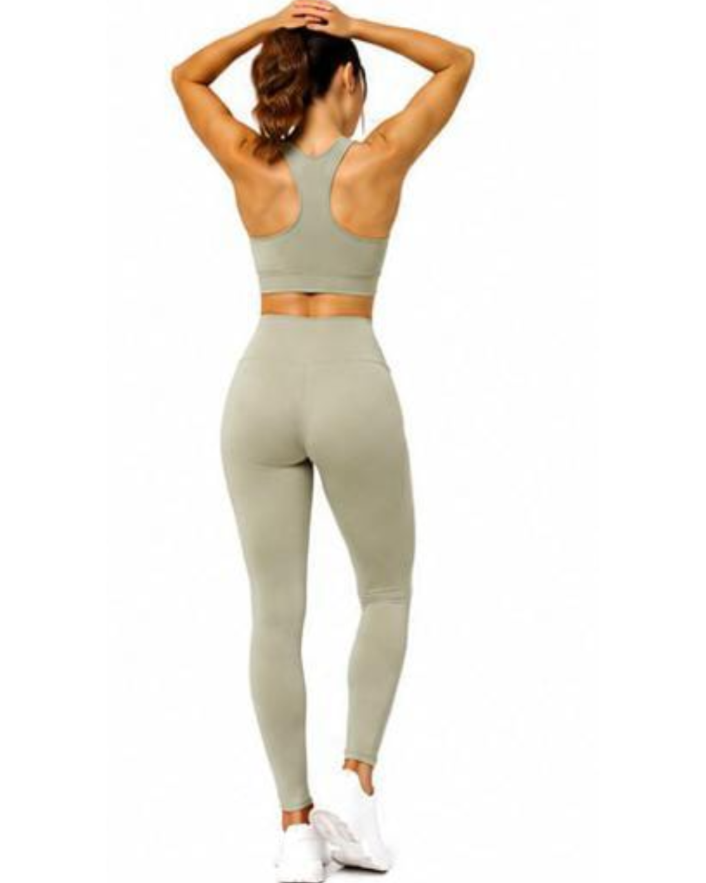 A woman shown from the back wearing a matching light sage green activewear set, consisting of a sports bra and high-waisted leggings, paired with white sneakers against a plain white background.