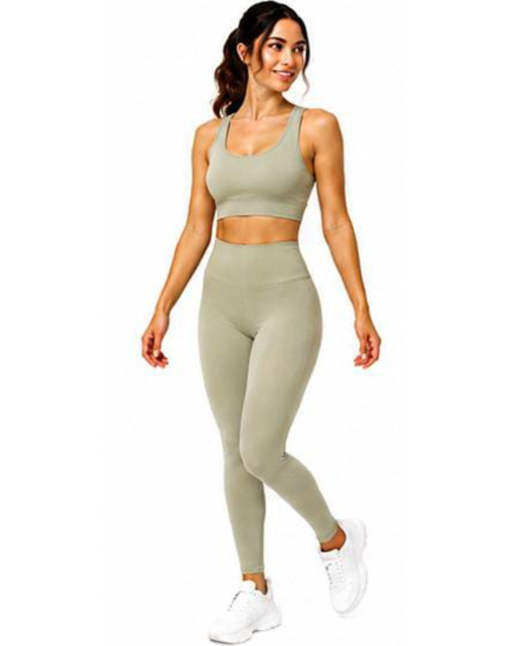 A woman modeling a matching two-piece activewear set in a light sage green color, consisting of a sports bra and high-waisted leggings, paired with white sneakers on a solid white background.