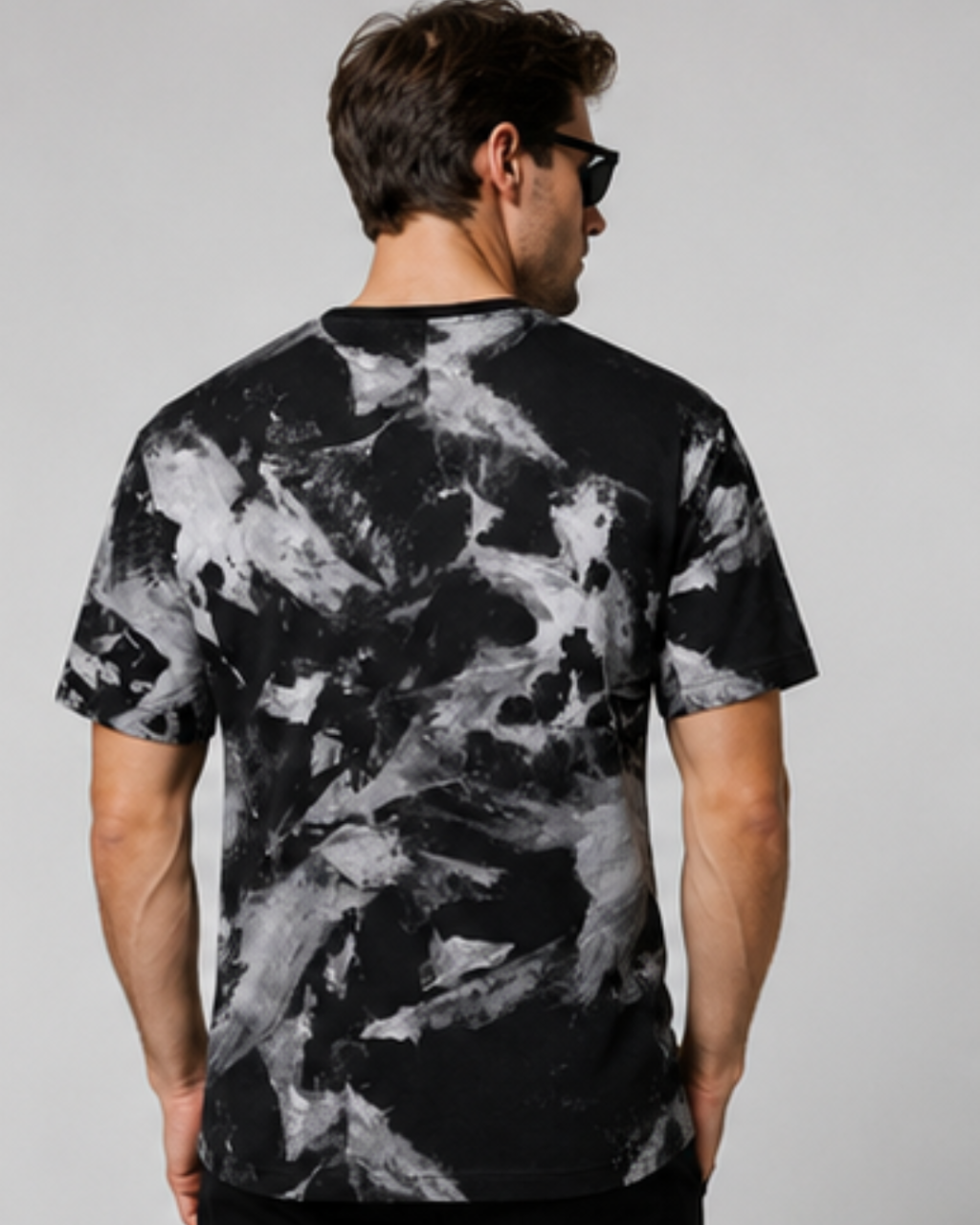 A man viewed from the back wearing a black short-sleeve t-shirt with a bold white marble or paint-splatter pattern, set against a plain light gray background.