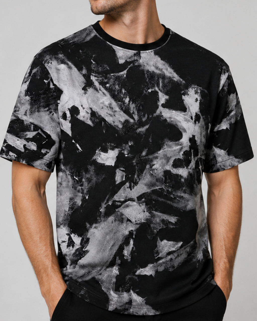 A man wearing a black short-sleeve crewneck t-shirt with a gray and white abstract paint splatter pattern, shown from the neck down against a neutral gray background.