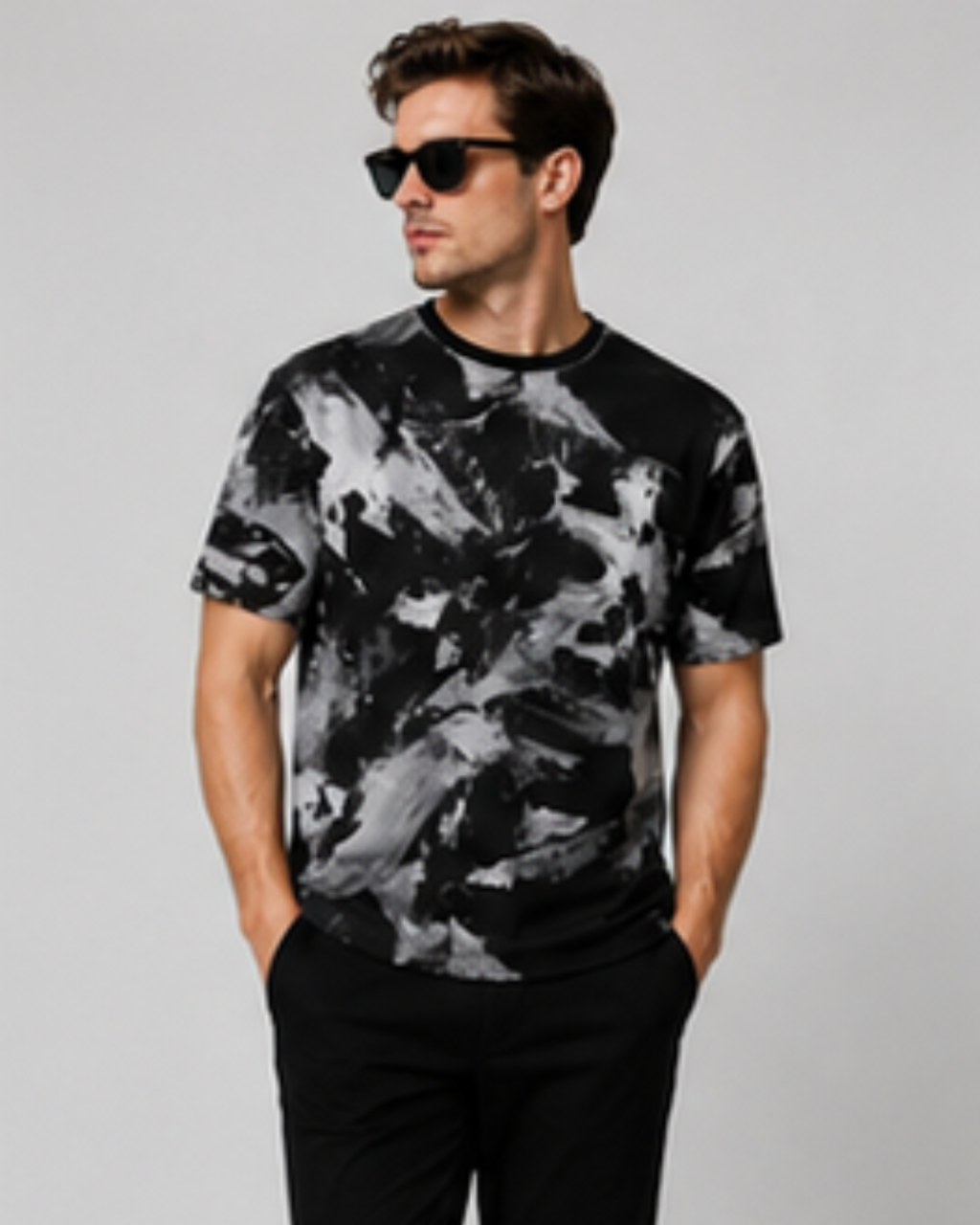 A man wearing a black and gray abstract print t-shirt and black pants, standing against a light gray studio background.