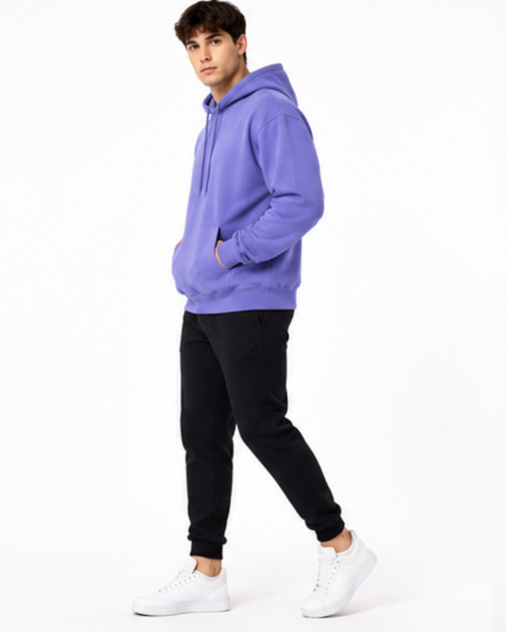 A man wearing a lavender-purple pullover hoodie, black jogger pants, and white sneakers, standing in profile against a plain white studio background.