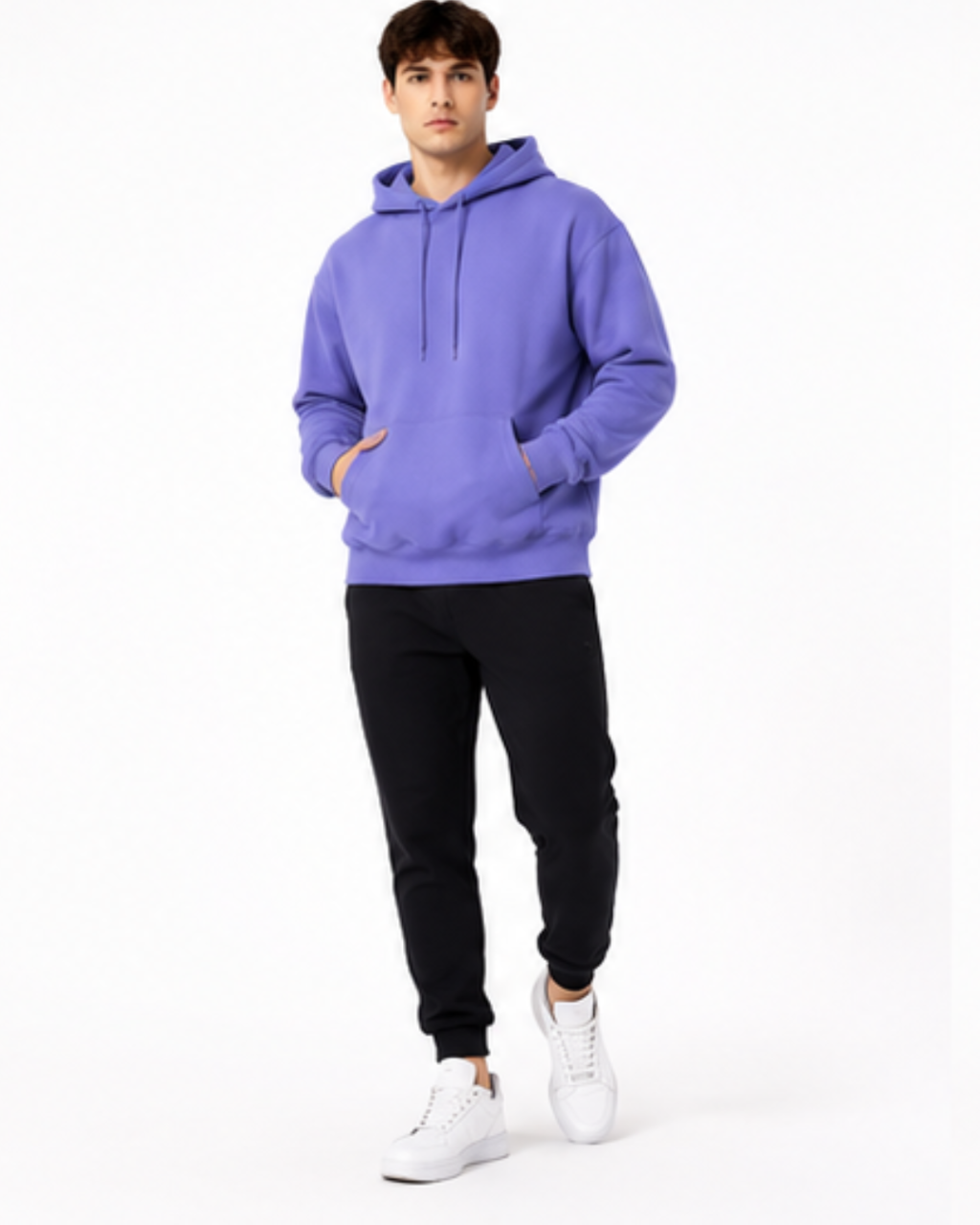 A man modeling a purple pullover hoodie with black jogger pants and white sneakers, standing against a plain white studio background.