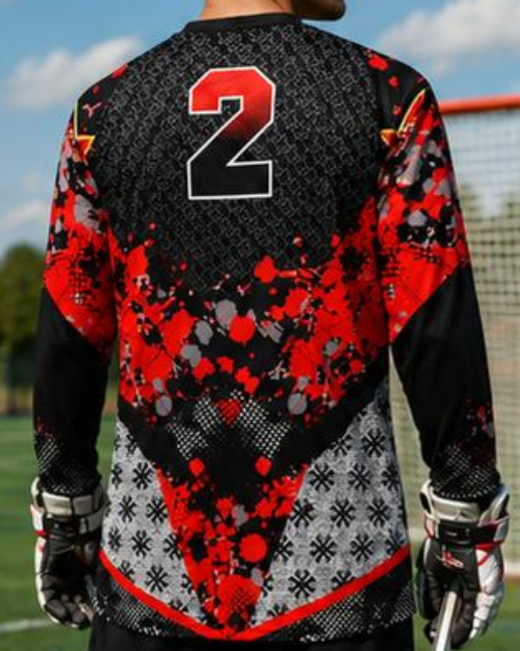 A long-sleeve soccer goalkeeper jersey shown from the back, featuring a black and red abstract splatter pattern with a large number 2 on the upper back, worn by a model on an outdoor field.