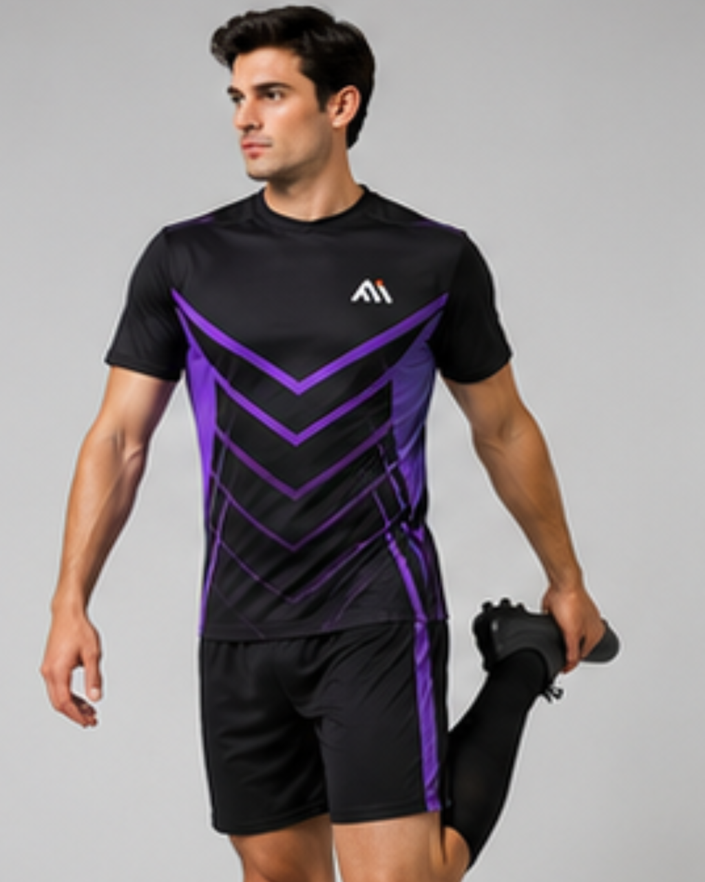 A man wearing a black athletic t-shirt with purple chevron patterns and matching black athletic shorts, stretching his leg against a solid gray background.