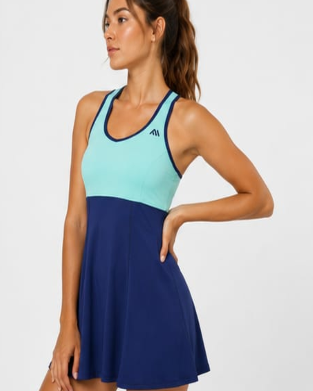 A woman modeling a colorblock athletic tennis dress with a light blue upper section and a navy blue flared skirt, set against a plain light gray background.