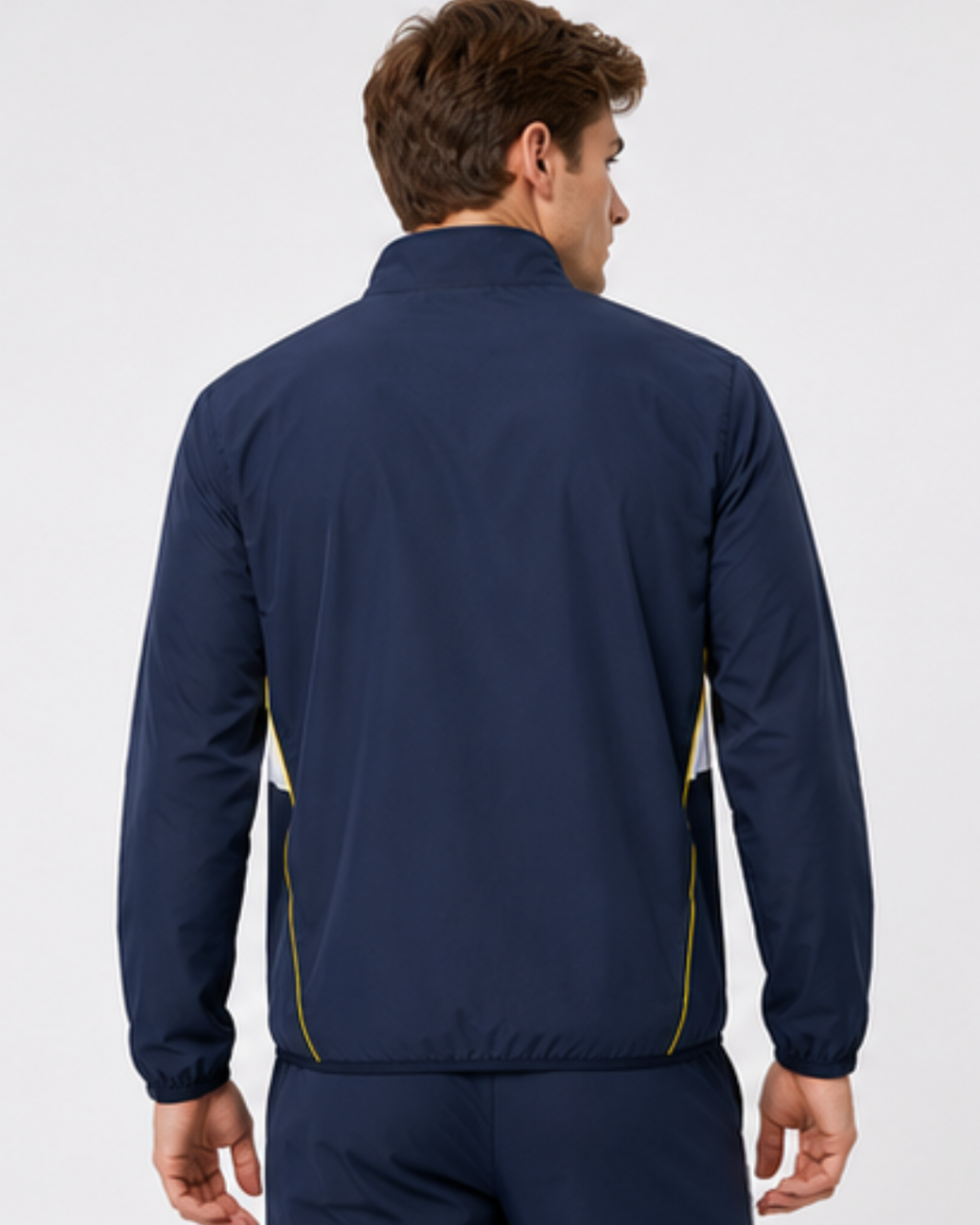 A man shown from the back wearing a navy blue zip-up athletic jacket with yellow piping details along the sides, set against a plain light gray studio background.