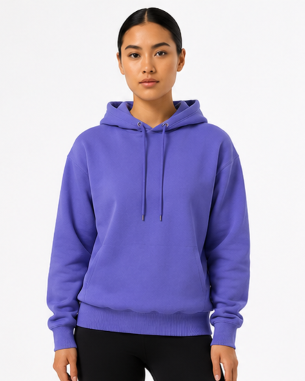 A woman modeling a solid purple pullover hoodie with black drawstrings, paired with black pants, against a clean white studio background.